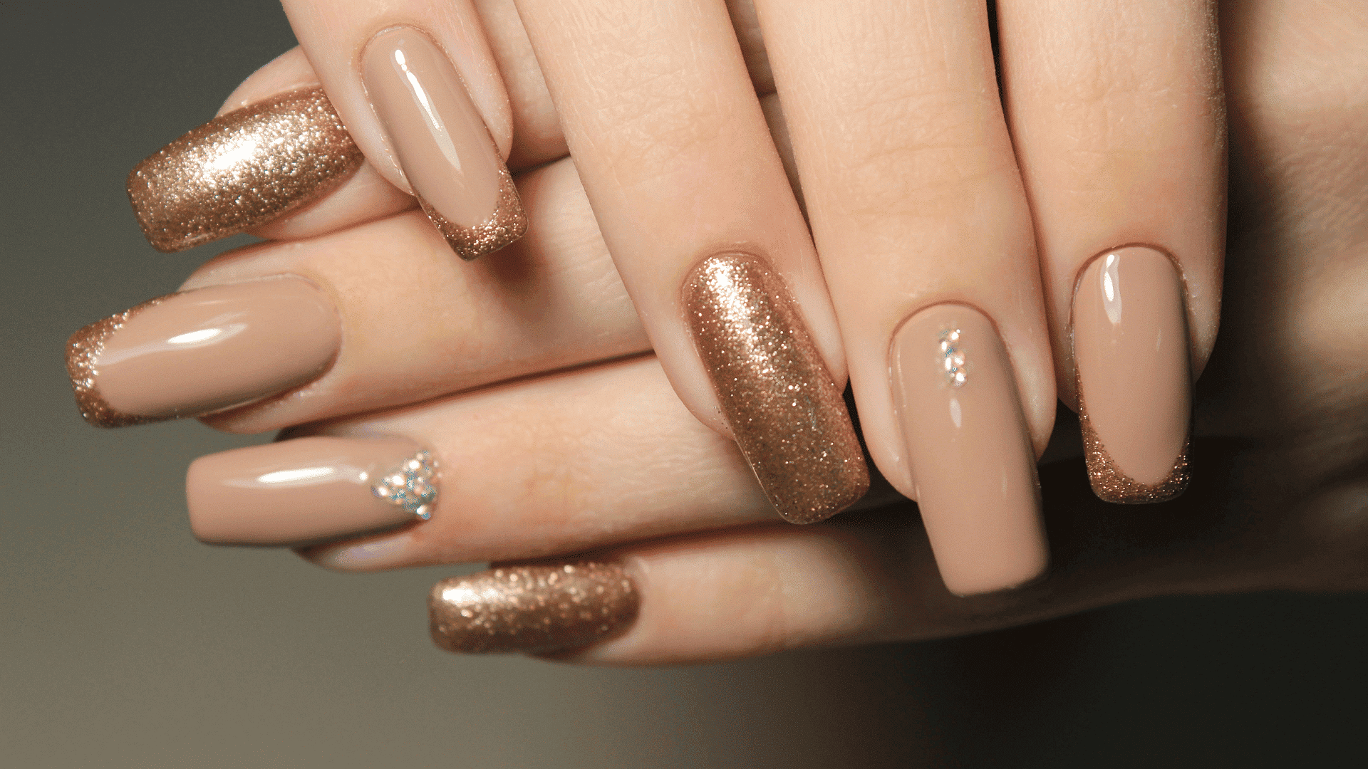 Elegant nude and gold glitter manicure with rhinestone accents.