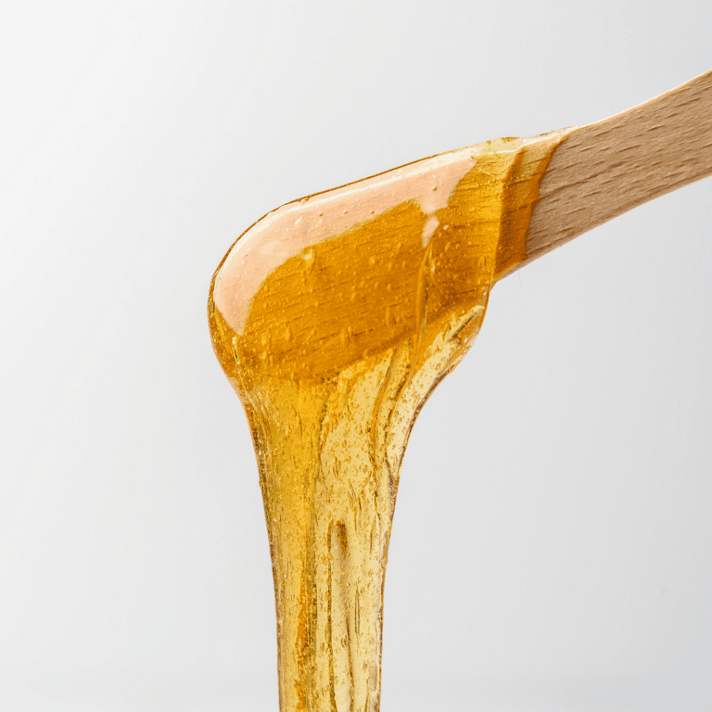 Honey drizzling from a wooden dipper against a light background.