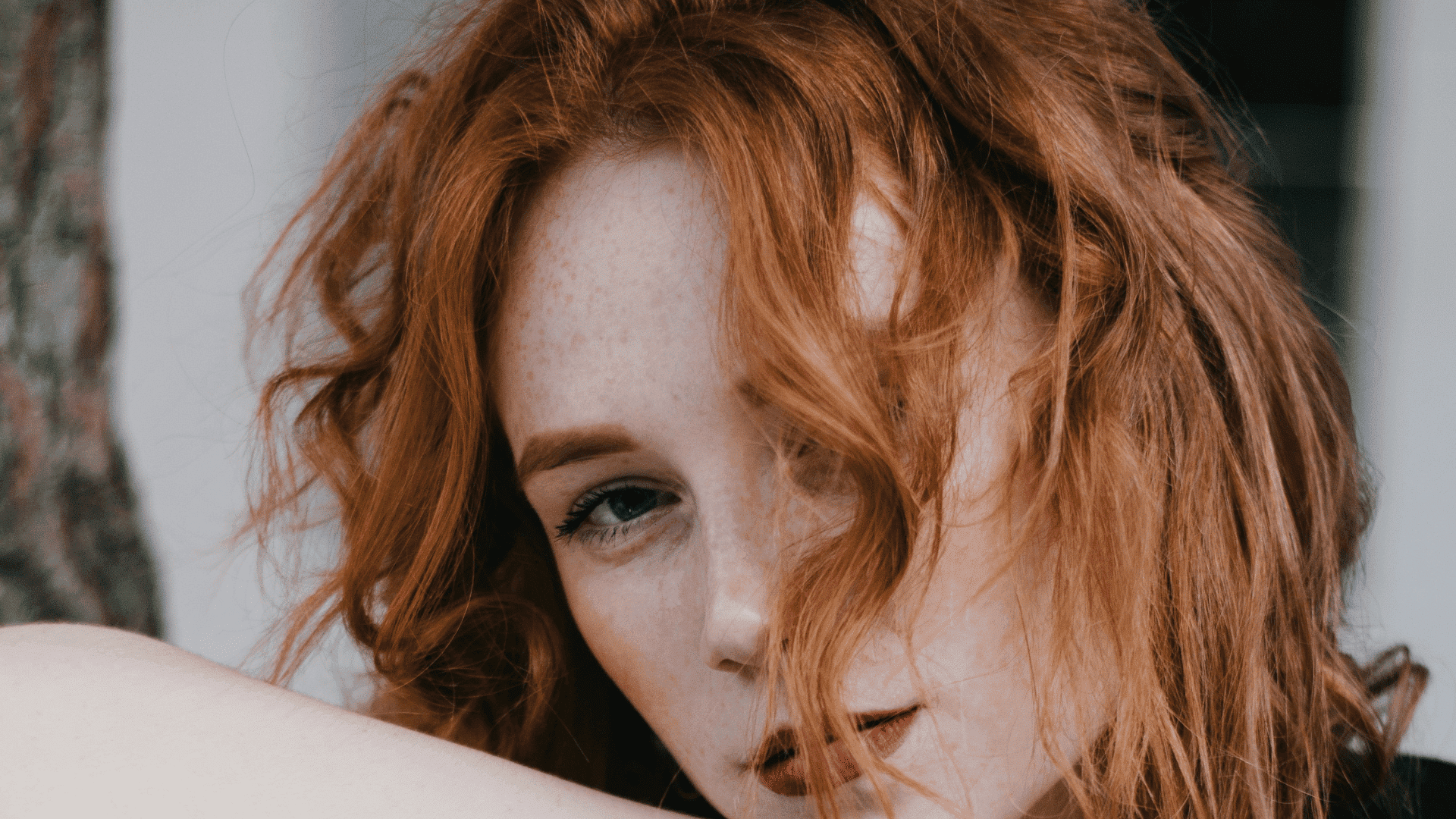 Red-haired person with wavy hair and freckles, looking towards the camera.